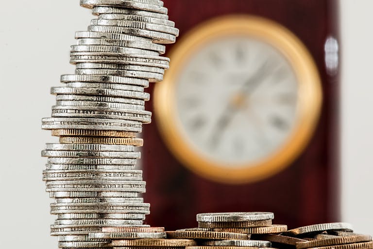 A close-up image of stacked coins with a blurred clock, symbolizing time and money relationship.